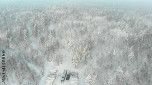 Industrial wood production concept: a log loader or forestry machine loads a log truck in winter, aerial video. photo