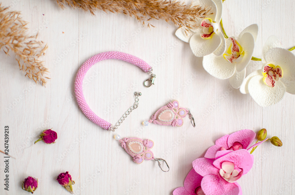Obraz premium Beaded braselet and earrings set. Pink soutache jewelry with flowers on the white wooden background. Women accessories