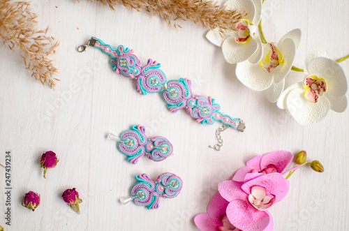 Fototapeta Naklejka Na Ścianę i Meble -  Beaded braselet and earrings set. Pink and blue soutache jewelry with flowers on the white wooden background. Women accessories