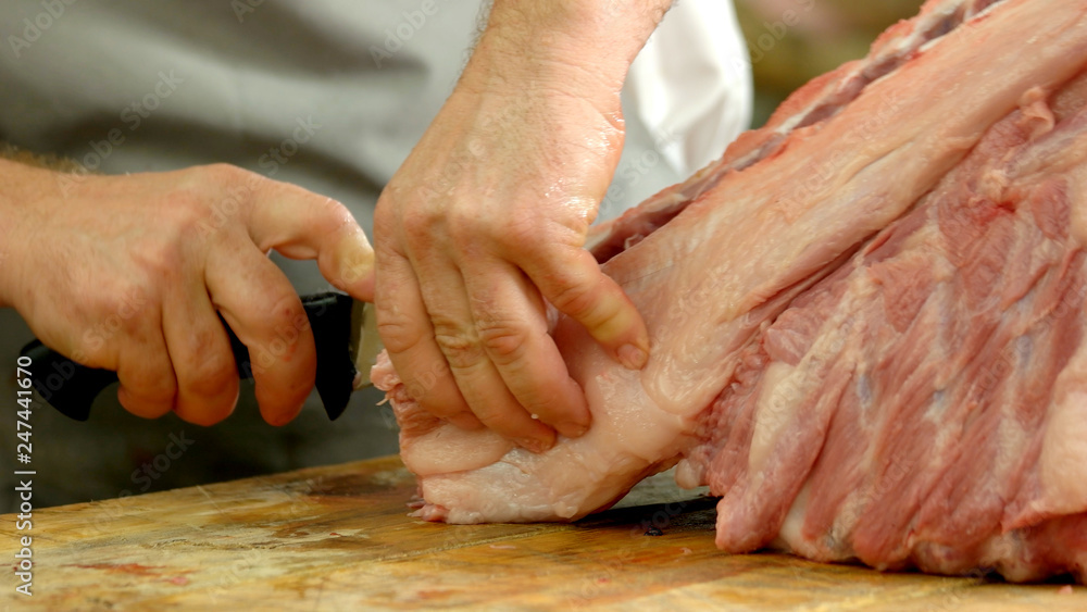 Close up of butchers hands cutting pork in butchers shop. Fresh raw meat at butchery. Production of healthy meat at factory.