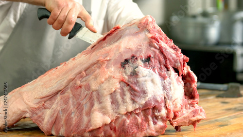 Splitting of pig carcass close up. Butcher cutting up a large slab of raw meat carcass with a knife. Processing a pig at home.