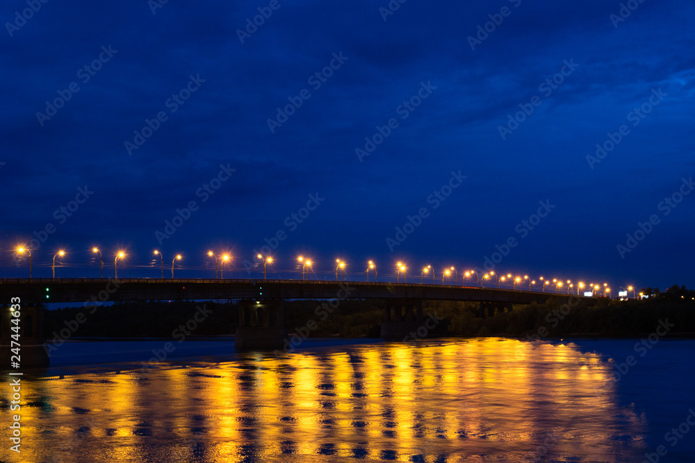A bridge is over the river in the evening. View is of the embankment, sity is Omsk, Russia