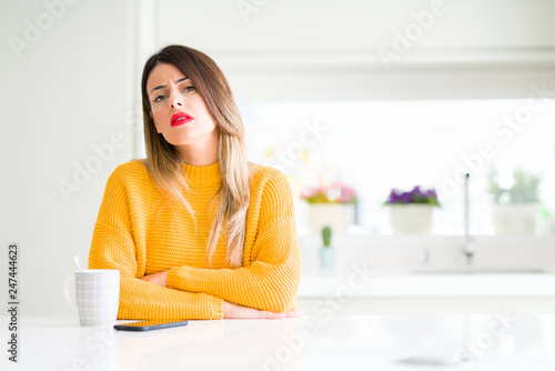 Young beautiful woman drinking a cup of coffee at home skeptic and nervous  disapproving expression on face with crossed arms. Negative person.