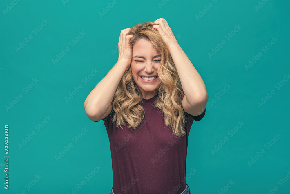 Attractive angry blonde girl angrily holds her head. Angry young woman on a blue background.