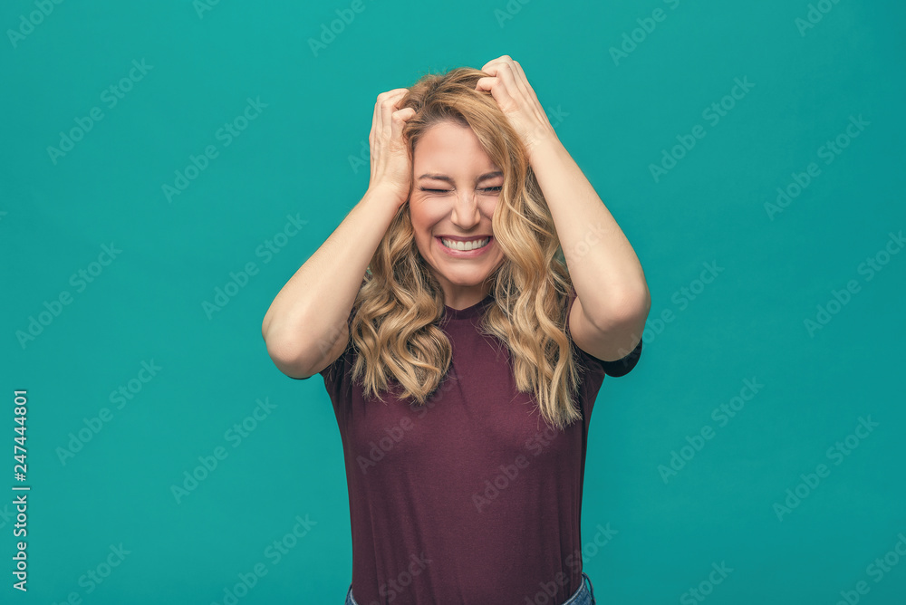 Attractive angry blonde girl angrily holds her head. Angry young woman on a blue background. Attractive angry blonde girl angrily holds her head. Angry young woman on a blue background.