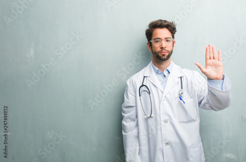 Young friendly doctor man against a grunge wall with a copy space serious and determined, putting hand in front, stop gesture, deny concept