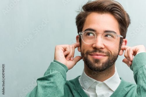 Young handsome entrepreneur man face closeup covering ears with hands, angry and tired of hearing some sound