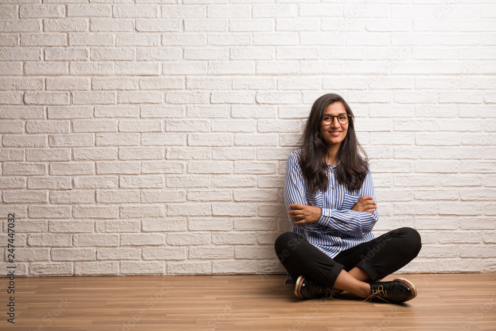 Young indian woman sit against a brick wall crossing his arms, smiling and happy, being confident and friendly Young indian woman sit against a brick wall crossing his arms, smiling and happy, being confident and friendly