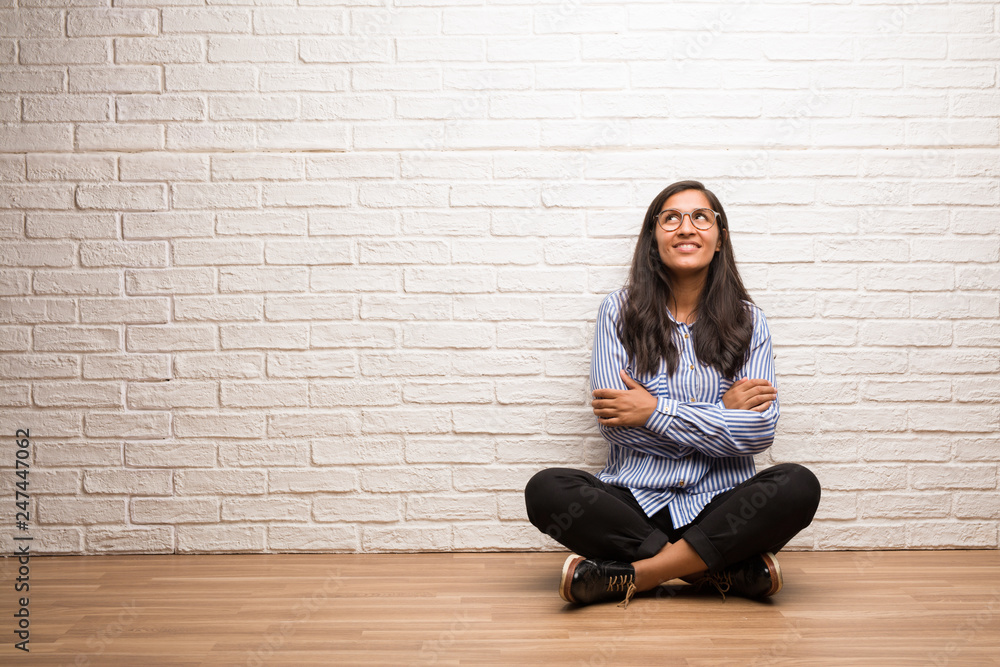 Young indian woman sit against a brick wall looking up, thinking of something fun and having an idea, concept of imagination, happy and excited Young indian woman sit against a brick wall looking up, thinking of something fun and having an idea, concept of imagination, happy and excited