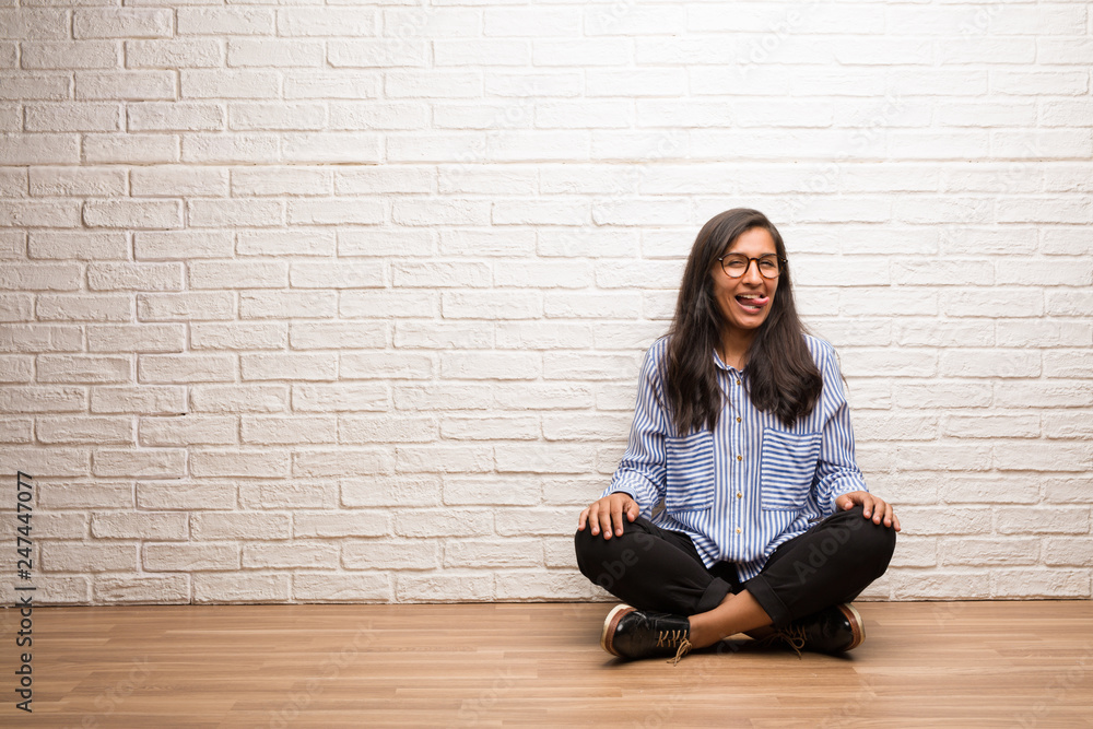 Young indian woman sit against a brick wall expression of confidence and emotion, fun and friendly, showing tongue as a sign of play or fun Young indian woman sit against a brick wall expression of confidence and emotion, fun and friendly, showing tongue as a sign of play or fun