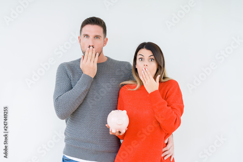 Young couple holding piggy bank over isolated background cover mouth with hand shocked with shame for mistake, expression of fear, scared in silence, secret concept