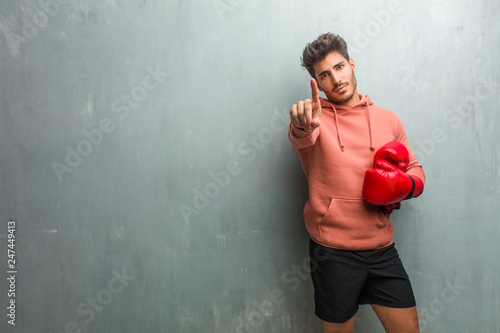 Young fitness man against a grunge wall showing number one, symbol of counting, concept of mathematics, confident and cheerful. © Asier