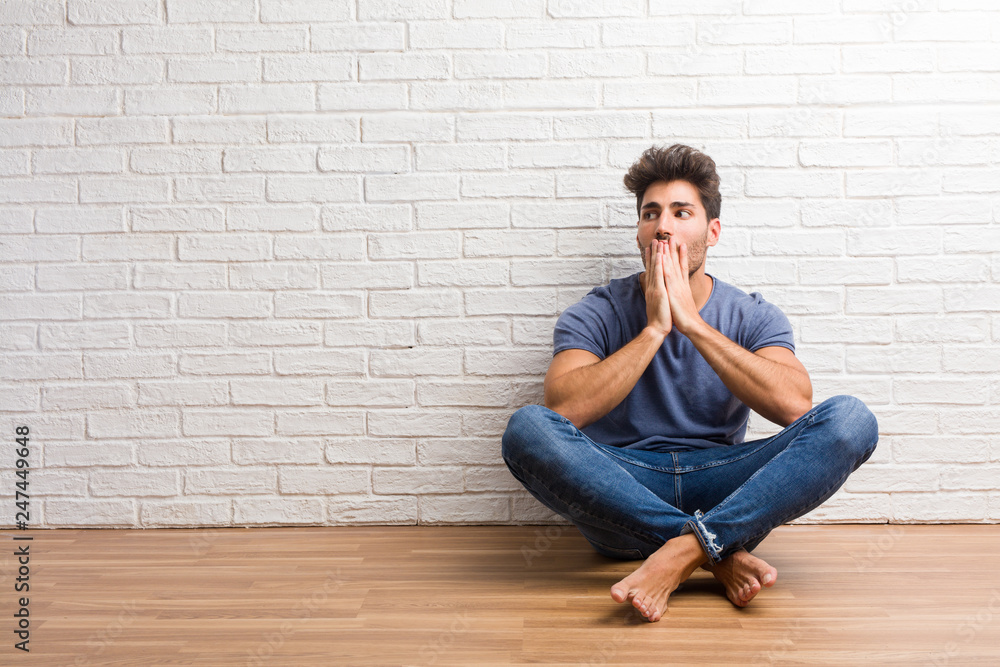 Young natural man sit on a wooden floor surprised and shocked, looking with wide eyes, excited by an offer or by a new job, win concept Young natural man sit on a wooden floor surprised and shocked, looking with wide eyes, excited by an offer or by a new job, win concept