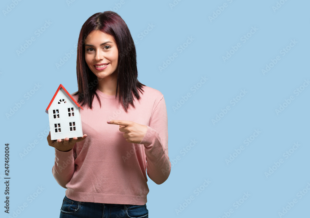 Young pretty woman happy and confident, showing a miniature house model, trying to sell it, concept of home and family Young pretty woman happy and confident, showing a miniature house model, trying to sell it, concept of home and family