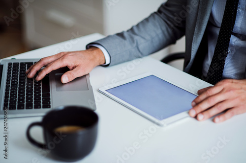 A midsection of businessman sitting at the table, using tablet. Copy space.