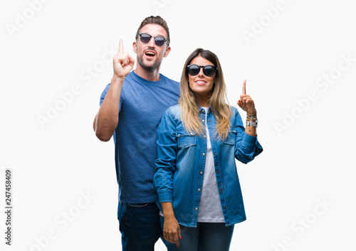 Young couple in love wearing sunglasses over isolated background pointing finger up with successful idea. Exited and happy. Number one.