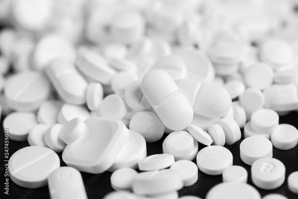 White pills or capsules on a black background White pills or capsules on a black background