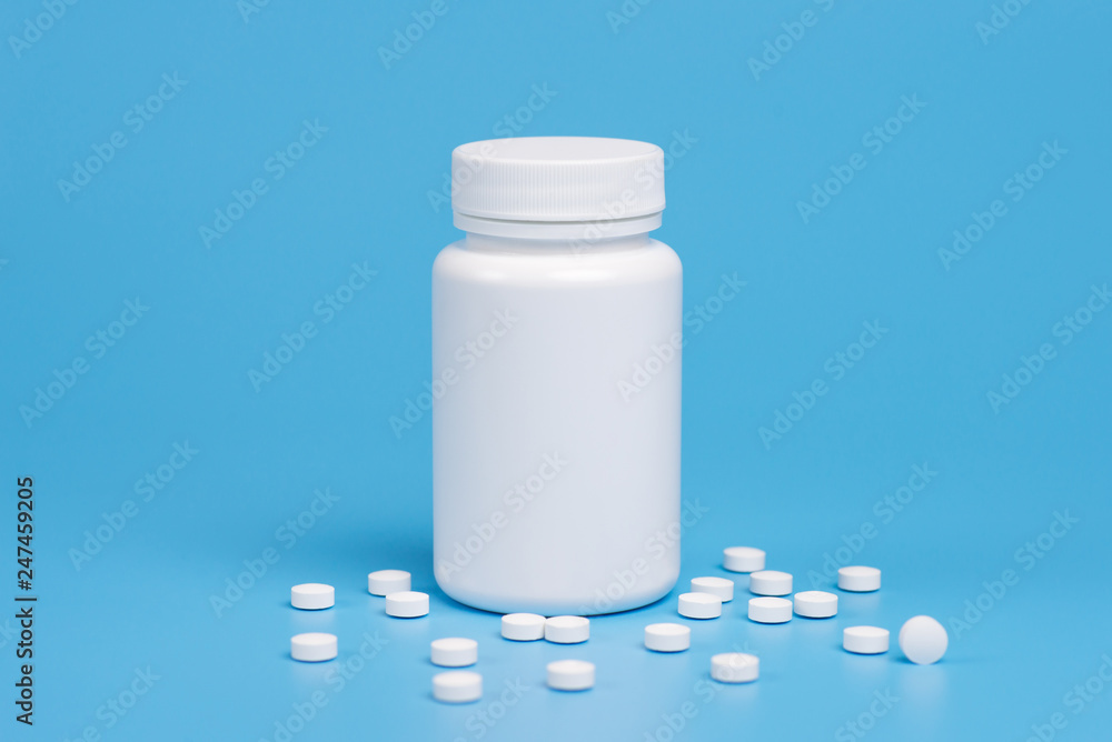 White pills, tablets and white bottle on blue background. White pills, tablets and white bottle on blue background.