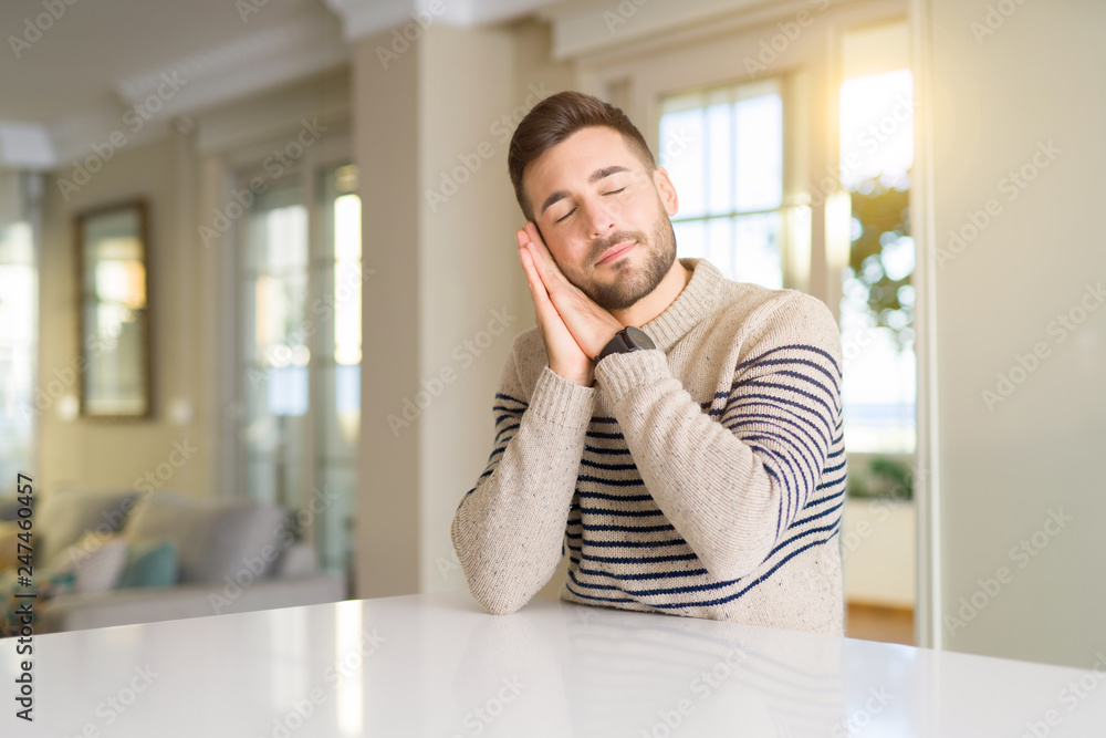 Fototapeta premium Young handsome man at home sleeping tired dreaming and posing with hands together while smiling with closed eyes.