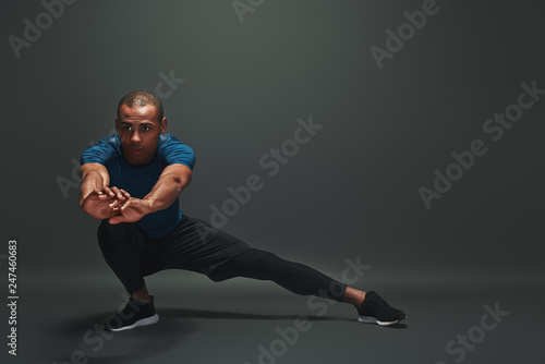 Always in a great shape. Sportsman is stretching standing over dark background