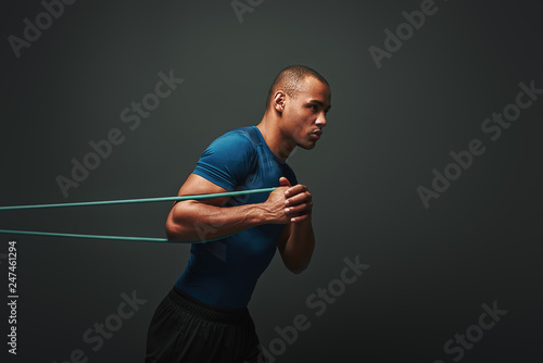 Pushing hard. Sportsman working out with resistance band over dark background