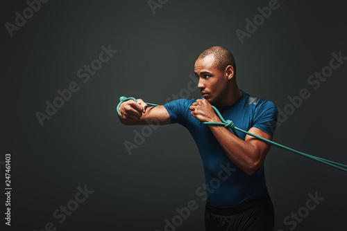 Sport is my lifestyle. Sportsman working out with resistance band over dark background
