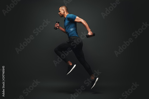 Fototapeta Naklejka Na Ścianę i Meble -  Everything you’ve ever wanted is on the other side of fear. Dark skinned sportsman jumping over dark background. He is ready to run