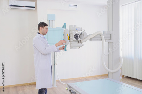  lateral view of a male radiologist adjusting the X-ray machine in examination rom