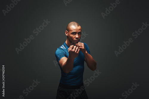 Come closer. Muscular boxer is ready to fight. Young sportsman standing over dark background