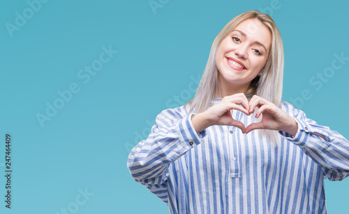 Young blonde woman over isolated background smiling in love showing heart symbol and shape with hands. Romantic concept.