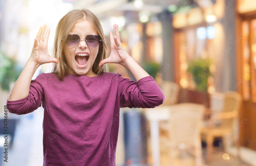 Fototapeta premium Young beautiful girl wearing sunglasses over isolated background celebrating mad and crazy for success with arms raised and closed eyes screaming excited. Winner concept