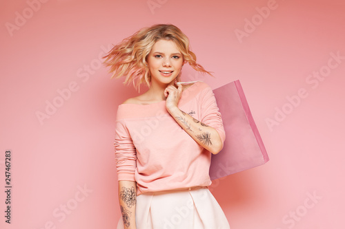 Young student hipster woman with colored flying hairs and tattoo holding shop bag. Isolated on the pink background