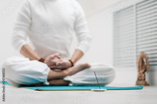 The concept of yoga and meditation. Close-up of the hands and feet of a man in white clothes on a light background.