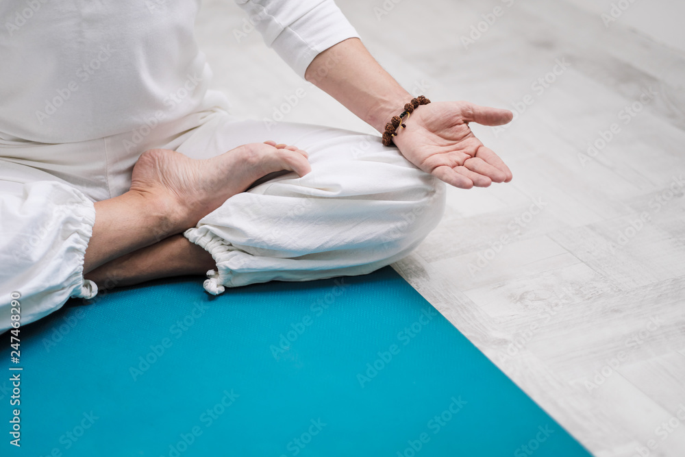 Concept of yoga and meditation. Close-up, hands of a man in white clothes, folded in prayer. White background and yellow-mini rubber mat.