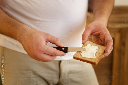 high-cholesterol food, unhealthy diet, bad carbs. overweight man spreading mayonnaise on bread.