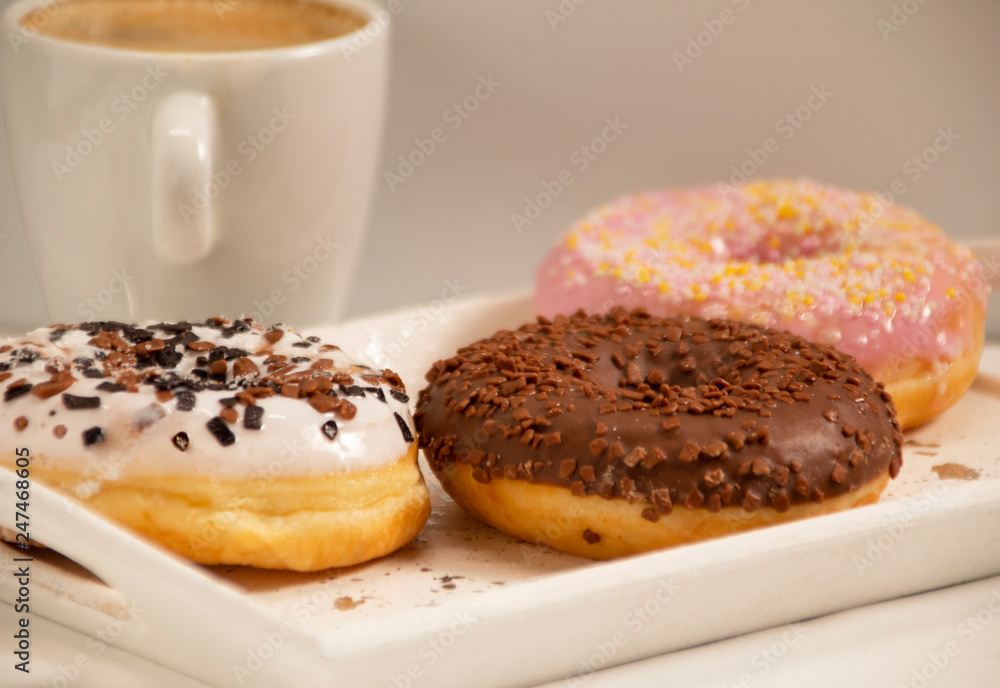 three donuts on a white tray with a cup of coffee
