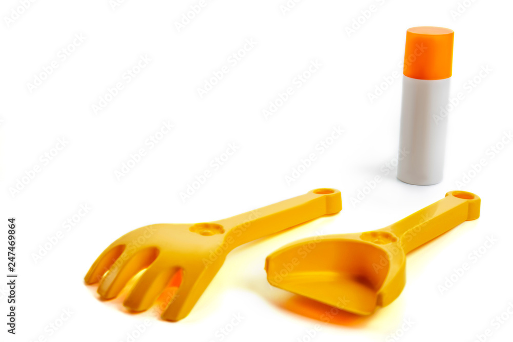 white bottle of suntan cream, forms for sand in the form of a rake, shovels lie on a white background, summer set white bottle of suntan cream, forms for sand in the form of a rake, shovels lie on a white background, summer set