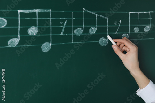 Woman writing music notes with chalk on blackboard, closeup
