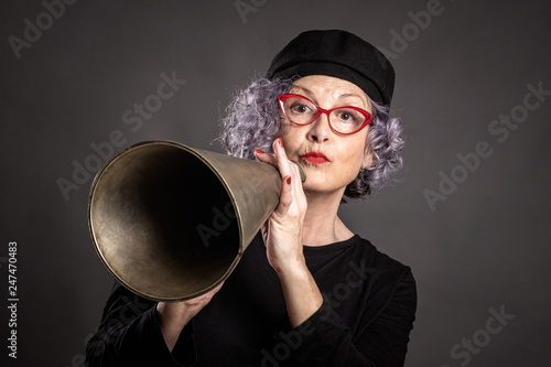 portrait of beautiful older woman shouting with an old megaphone on a gray background
