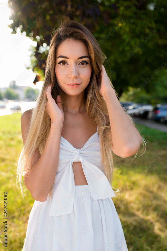 Young and beautiful girl in park with long hair. Portrait of woman summer outdoors. Tanned skin and casual makeup. Emotionally tender smile and insightful look. Hair straightens happy smiling rests.
