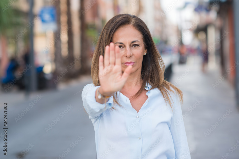 Beautiful middle age hispanic woman at the city street on a sunny day with open hand doing stop sign with serious and confident expression, defense gesture