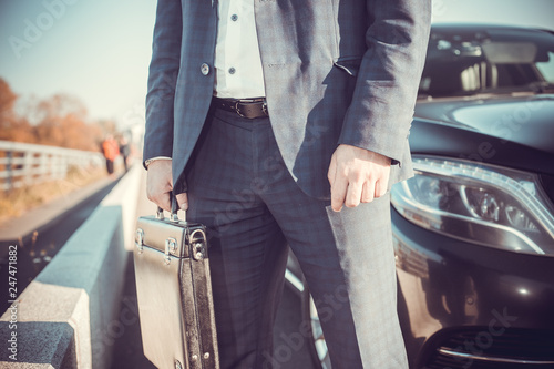  a businessman standing near in front of luxury car holding brief case or diplomat