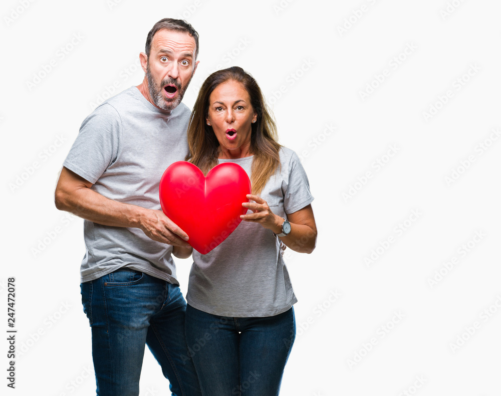 Middle age hispanic casual couple in love holding red heart over isolated background scared in shock with a surprise face, afraid and excited with fear expression Middle age hispanic casual couple in love holding red heart over isolated background scared in shock with a surprise face, afraid and excited with fear expression
