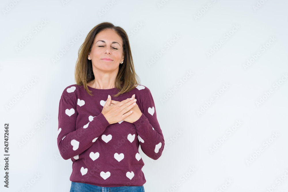 Beautiful middle age woman wearing heart sweater over isolated background smiling with hands on chest with closed eyes and grateful gesture on face. Health concept. Beautiful middle age woman wearing heart sweater over isolated background smiling with hands on chest with closed eyes and grateful gesture on face. Health concept.