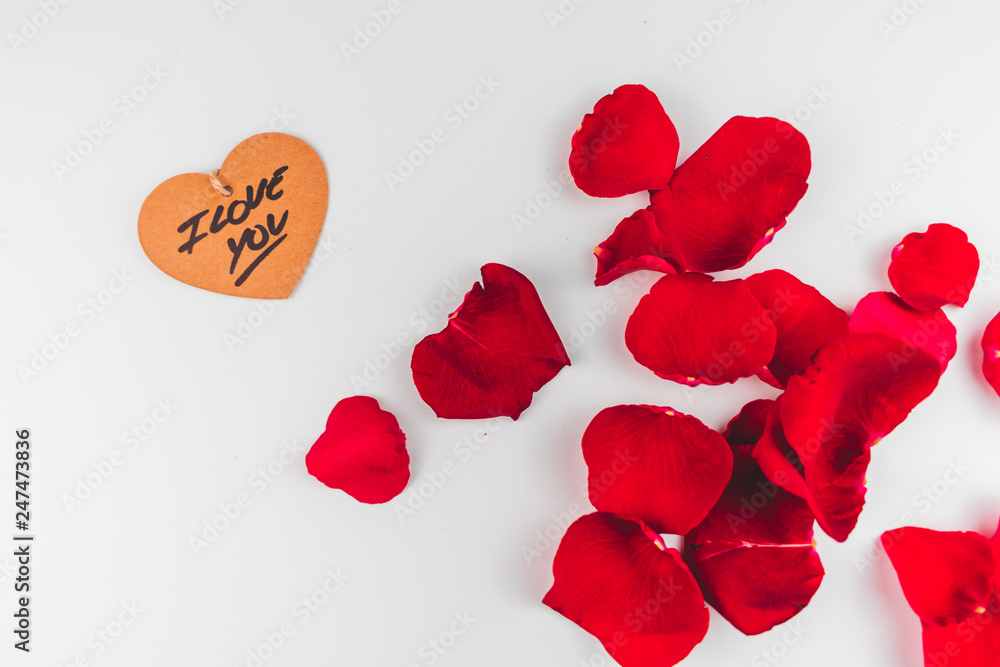 Fototapeta premium Etiqueta en forma de corazón y aislados con pétalos rojos en un fondo blanco