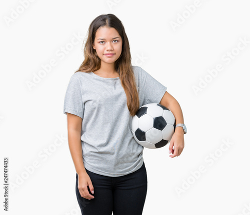 Young beautiful brunette woman holding soccer football ball over isolated background with a confident expression on smart face thinking serious