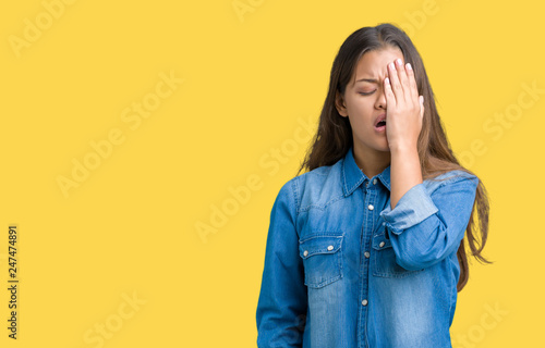 Young beautiful brunette woman wearing blue denim shirt over isolated background Yawning tired covering half face, eye and mouth with hand. Face hurts in pain.