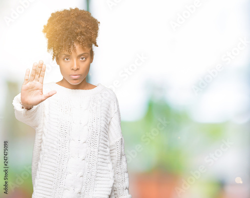 Beautiful young african american woman wearing winter sweater over isolated background doing stop sing with palm of the hand. Warning expression with negative and serious gesture on the face. © Krakenimages.com