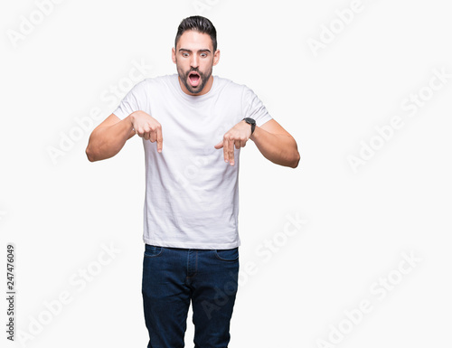 Handsome man wearing white t-shirt over white isolated background Pointing down with fingers showing advertisement, surprised face and open mouth