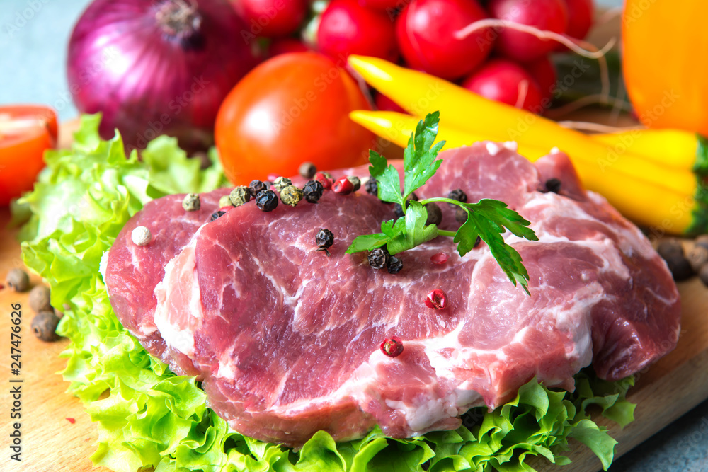 Pork-neck meat steaks on lettuce on background of radishes, tomato, red chili peppers, yellow chili peppers, green paprika, yellow paprika, red paprika, black pepper. Horizontal. Red onions, shallots Pork-neck meat steaks on lettuce on background of radishes, tomato, red chili peppers, yellow chili peppers, green paprika, yellow paprika, red paprika, black pepper. Horizontal. Red onions, shallots
